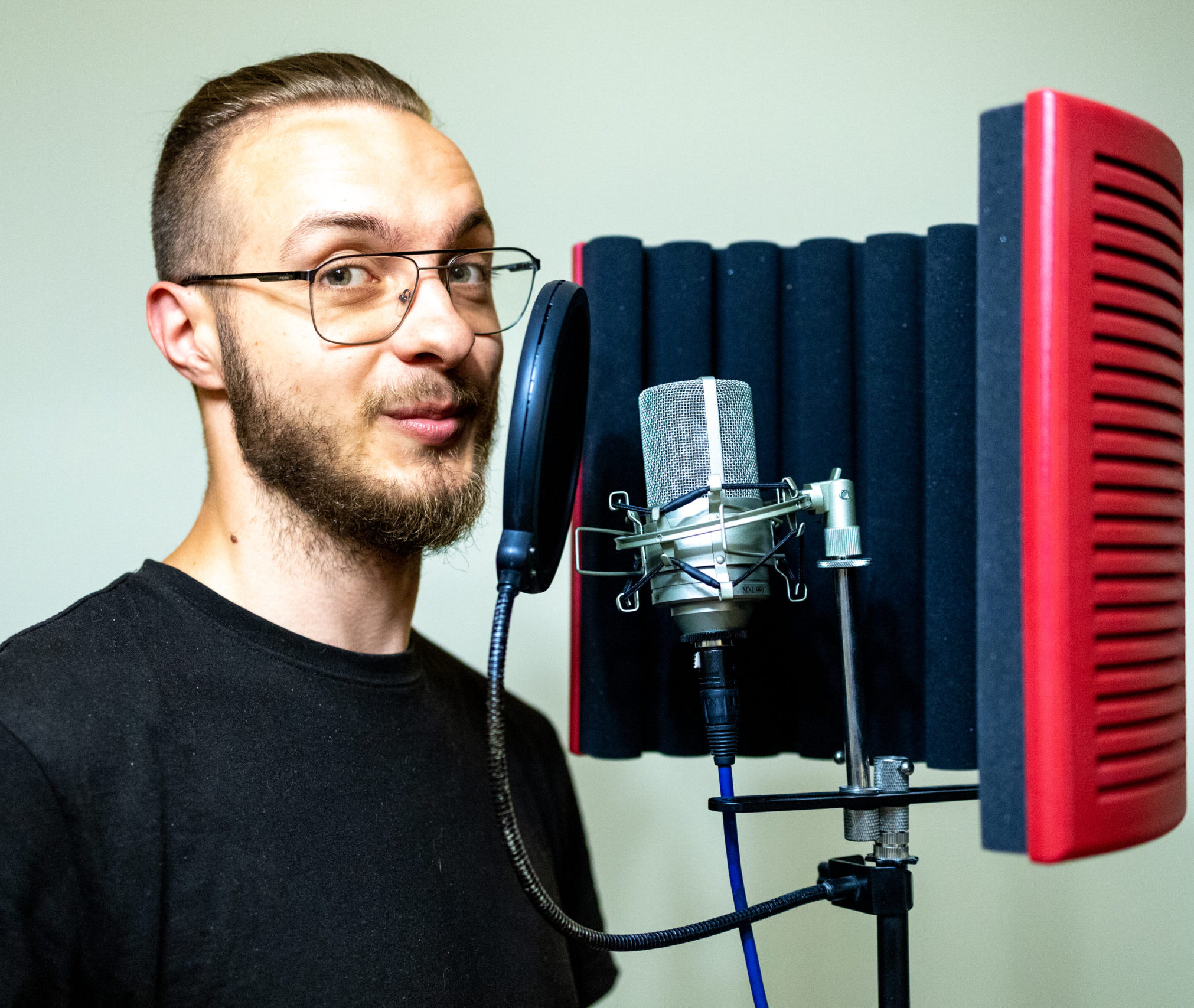 Mężczyzna w okularach nagrywający głos w studiu z mikrofonem pojemnościowym i ekranem akustycznym